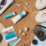 A collection of travel accessories, including sunglasses and a beach towel, arranged on a sandy beach